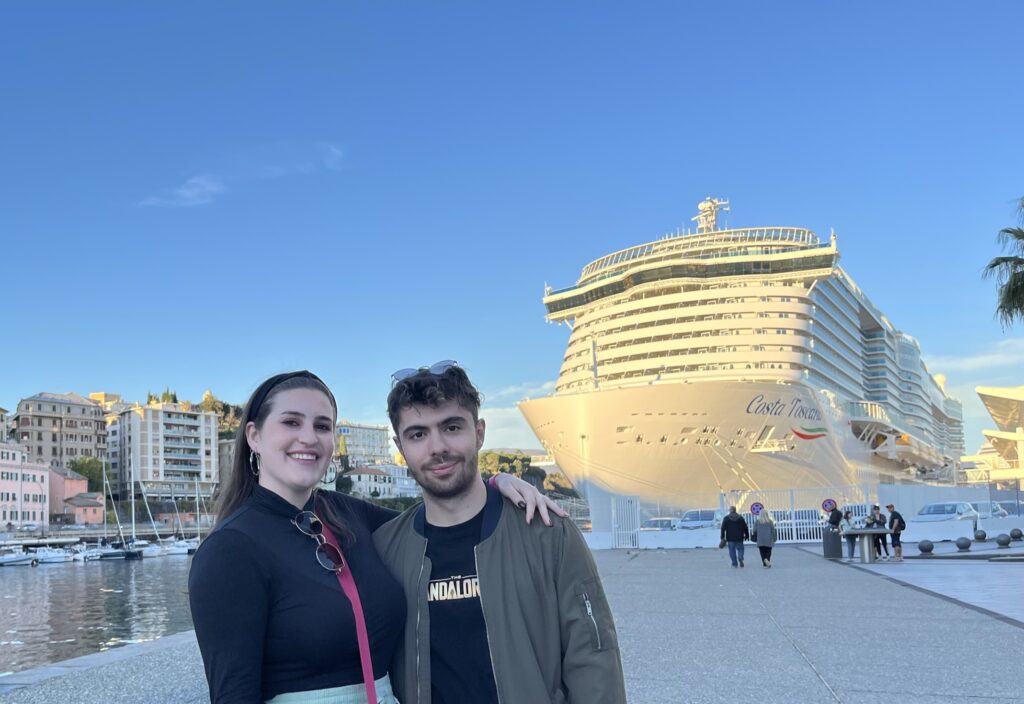 dos persona en un puerto, detrás de ellas hay un crucero y un pueblo